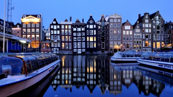 A nighttime image of a river in Amsterdam lined with buildings.